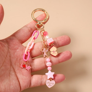 Detailed close-up of pink beaded star keychain with LOVE and Merry Me charms held in hand