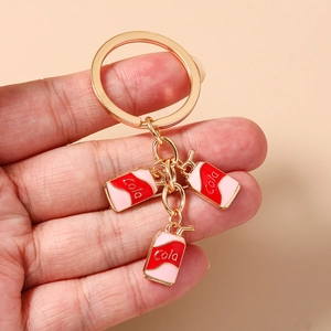 Close-up of golden keychain featuring red and pink miniature cola can charms on a hand