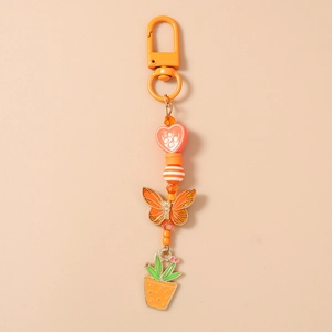 Détail du porte-clés à perles orange avec breloques papillon et cactus sur fond crème
