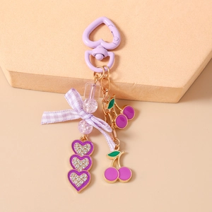 Detail of purple cherry and heart charms on a bow keychain with sparkling rhinestones