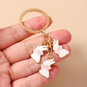 Vue détaillée du porte-clés doré avec trois lapins en émail blanc et nœuds roses