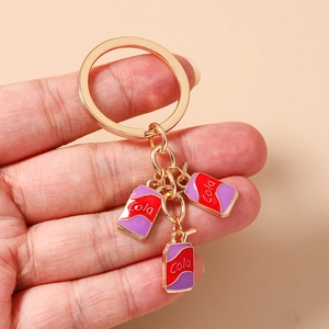 Close-up of golden keychain featuring miniature enamel cola can charms with straw details