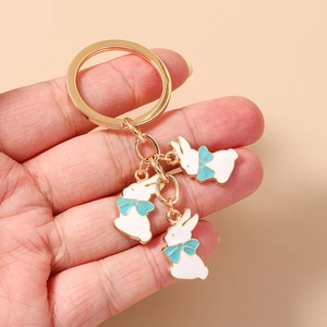 Gros plan d'un porte-clés doré avec trois lapins blancs et des nœuds papillon bleus