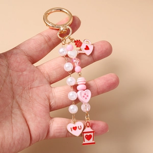 Detail of beaded keychain with pink heart, watering can and lamp charms on gold ring