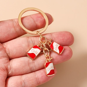 Detail view of cartoon cola can pendants on a gold keychain for bags and keys