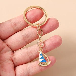 Detailed view of a golden enamel sailboat keychain with blue and white accents held in hand
