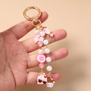 Pink beaded keychain with gold clasp, bow, and floral heart pendants held in hand