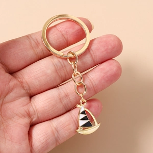 Detailed close-up of a golden sailing boat keychain with black and white enamel finish