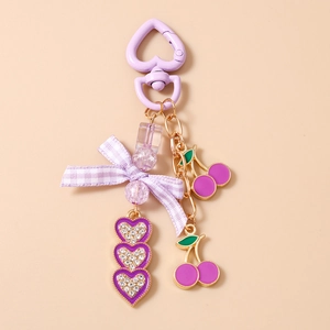 Detail of purple heart keychain with checkered bow and cherry pendants on beige surface