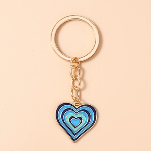 Détail du porte-clés cœur doré avec émail dégradé bleu sur un fond rose pastel