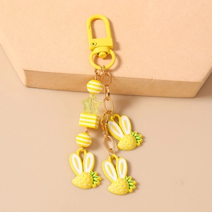 Dettaglio portachiavi a coniglio giallo con catena dorata e perle a righe su base beige