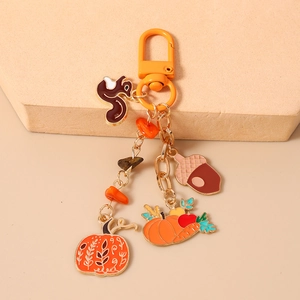 Detailed view of enamel squirrel, acorn, and pumpkin charms on a gold autumn keychain