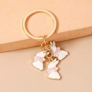 Détail de trois breloques lapin blanc avec nœuds roses sur un porte-clés doré