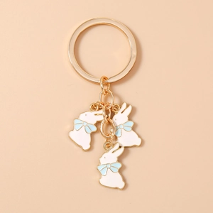 Détail de trois pendentifs lapin blancs avec nœuds bleus sur un porte-clés doré