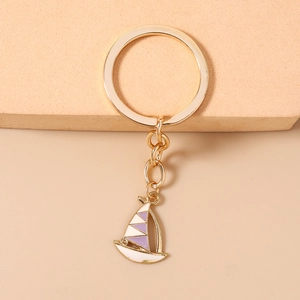 Detail view of golden sailboat keychain with white and purple enamel geometric design