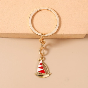 Close-up of golden sailboat keychain with red and white enamel detailing on sails