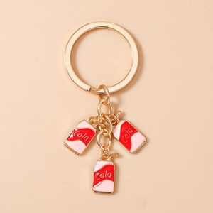Close-up of golden keychain with cute red and pink enamel soda can charms labeled Cola