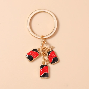 Detail of three miniature cola can pendants in red and black on golden metal keychain