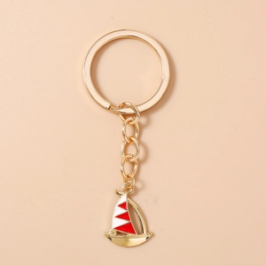 Detail of creative golden sailboat keychain with red and white enamel finish and keyring