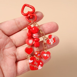 Detailed view of red heart keychain featuring beaded charms and Be Lovely enamel tags