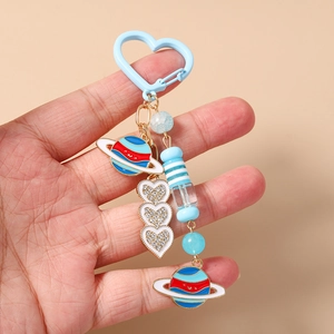 Gros plan d'un porte-clés bleu en forme de cœur avec perles et planètes à la main