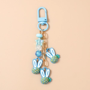Dettaglio dei ciondoli ananas con orecchie di coniglio e perline su un portachiavi blu cobalto