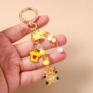 Vue détaillée d'un porte-clés doré avec un ours orange mignon, des perles et une petite robe