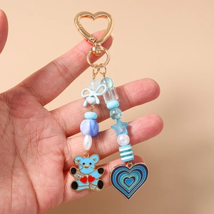 Detail of blue beaded keychain with cartoon bear charm and heart pendant held in hand
