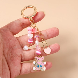 Détail d'un porte-clés ours avec émail rose et perles présenté à la main