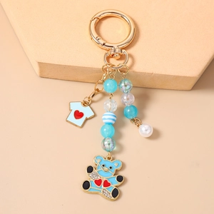 Détail du porte-clés perlé avec breloque ours bleu, strass et pendentif t-shirt en émail