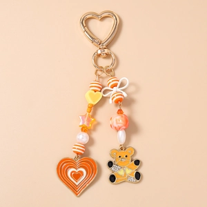 Detail view of orange cartoon bear keychain with golden heart clasp and beaded charms