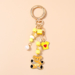 Détail d'un porte-clés doré avec pendentif ours jaune et perles élégantes pour sac