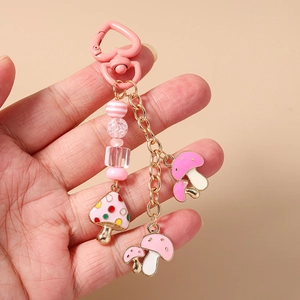 Porte-clés avec fermoir coeur rose et pendentif champignon tenu à la main sur fond beige