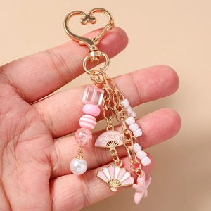 Pink starfish and fan charms on a golden heart clasp keychain held by hand