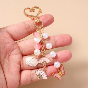 Detailed close-up of a golden keychain featuring pink fans, shell, and enamel butterfly charm