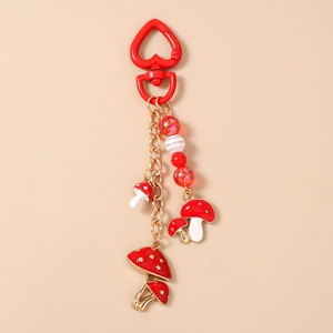 Détail d'un porte-clés champignon rouge avec mousqueton cœur et perles sur fond beige