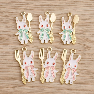 Set mit sechs Kaninchen-Emaille-Anhängern mit goldenen Löffeln und Gabeln auf Holz