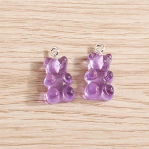 Macro shot of two transparent purple resin gummy bear charms with silver metal loops on wood