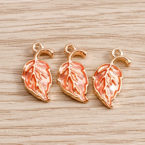 Detailed close-up of three orange enamel maple leaf charms with golden metal outlines