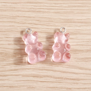 Macro shot of pink translucent resin gummy bear charms with silver hooks on wood background