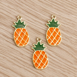 Detailed close-up of three pineapple enamel charms with gold trim on wooden background