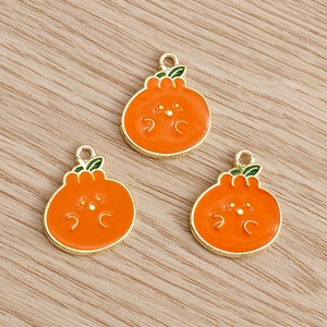 Three fruit-shaped enamel pendants with cute cartoon faces on a light wood background