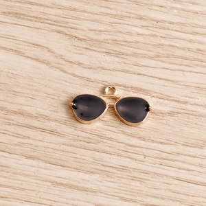 Detailed view of sunglasses-shaped golden alloy pendants with black enamel for DIY jewelry