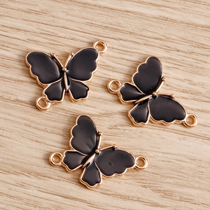 Three gold-plated alloy butterfly charms with black enamel finish on light wood background