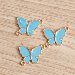 Three blue enamel butterfly connectors with double hanging loops on wooden background