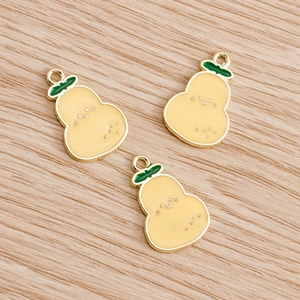 Detailed close-up of three yellow enamel pineapple pendants with faces on wood background
