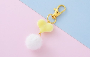 Dettaglio del ciondolo a cuore con pompon bianco e chiusura in metallo dorato lucido