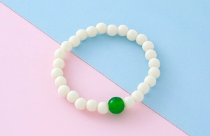 Gros plan de perles blanches mates avec une agate verte centrale sur un bracelet extensible