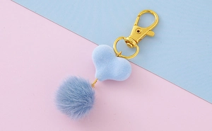 Dettaglio con pompon blu e ciondolo a cuore floccato con chiusura a moschettone
