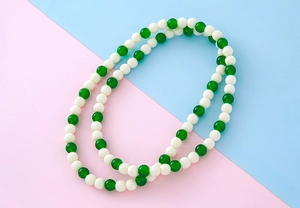 Détail d'un collier de perles vertes et blanc crème sur un fond bicolore éclatant